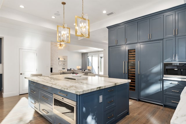 kitchen with light stone countertops, built in microwave, dark wood-type flooring, blue cabinetry, and hanging light fixtures