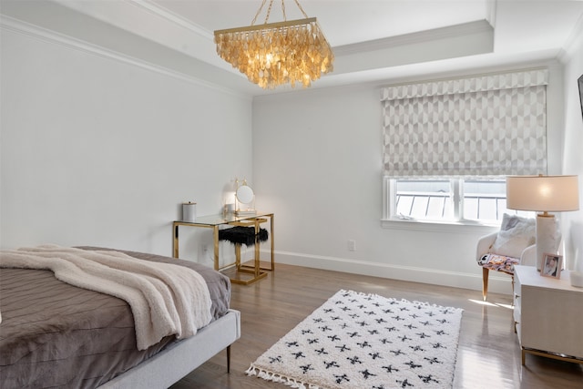 bedroom with hardwood / wood-style floors, a notable chandelier, ornamental molding, and a tray ceiling