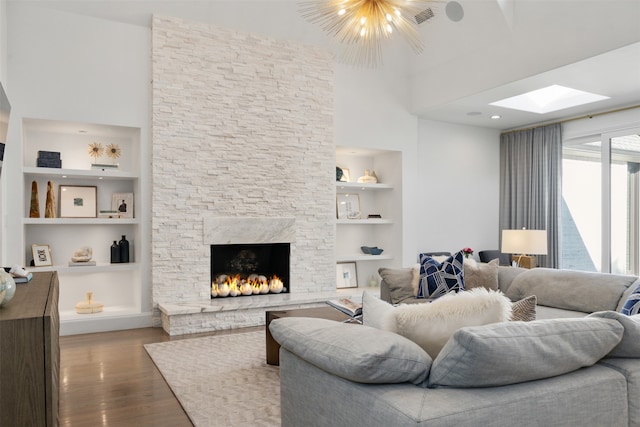 living room with a stone fireplace, built in shelves, wood-type flooring, and an inviting chandelier