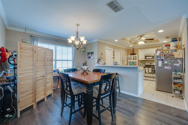 dining space featuring ceiling fan with notable chandelier, light hardwood / wood-style floors, a raised ceiling, and crown molding