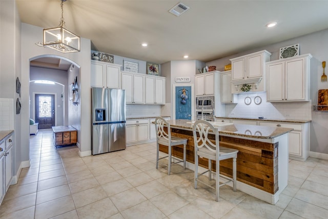 kitchen with white cabinetry, hanging light fixtures, an inviting chandelier, a center island with sink, and appliances with stainless steel finishes