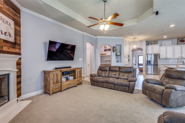 carpeted living room featuring a tray ceiling, ceiling fan, and ornamental molding