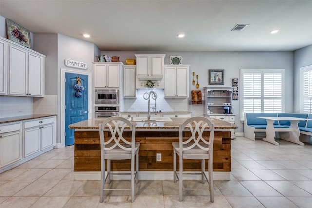 kitchen featuring a kitchen breakfast bar, light stone counters, backsplash, an island with sink, and appliances with stainless steel finishes