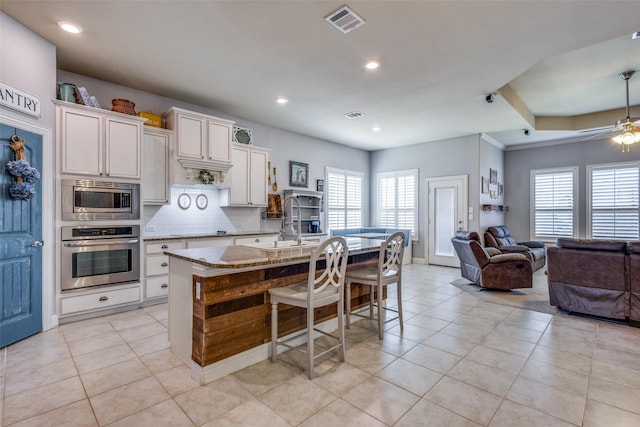 kitchen with light stone countertops, stainless steel appliances, a kitchen bar, a center island with sink, and white cabinets