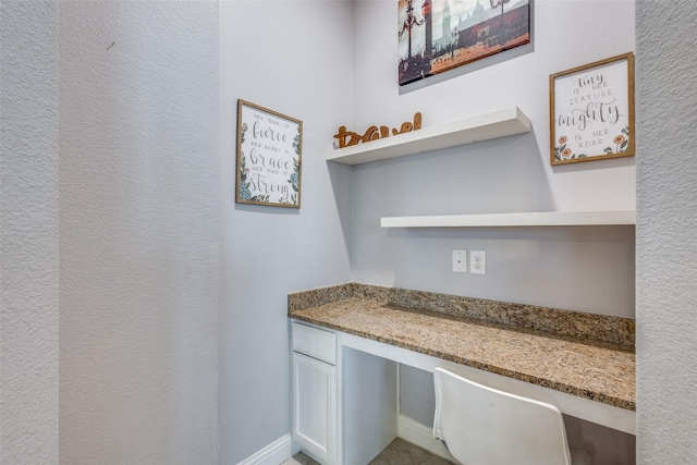 interior space featuring white cabinets, built in desk, and stone countertops