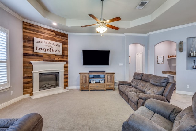 carpeted living room featuring a tray ceiling, ceiling fan, crown molding, and wood walls