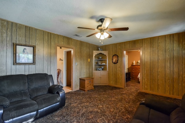 living room with a textured ceiling, carpet, wood walls, and ceiling fan