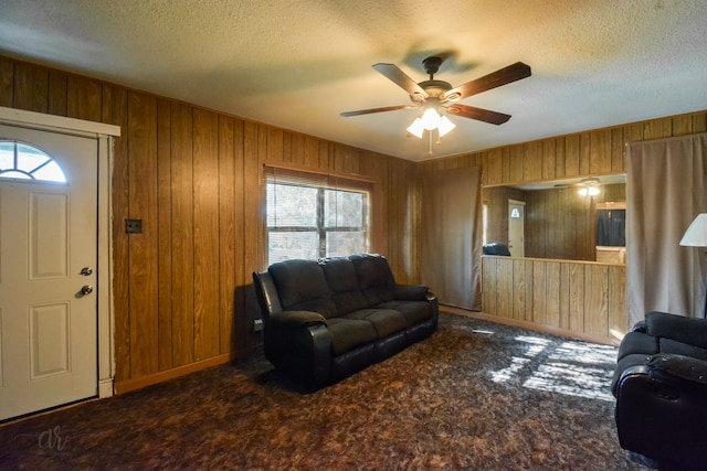 carpeted living room featuring a textured ceiling, wood walls, and ceiling fan