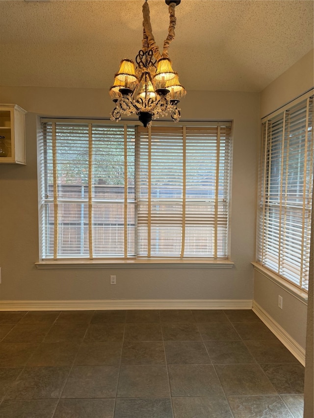 unfurnished dining area featuring a textured ceiling, a chandelier, and dark tile patterned floors