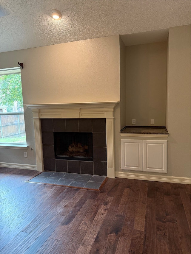 unfurnished living room featuring a textured ceiling, dark hardwood / wood-style flooring, and a tile fireplace