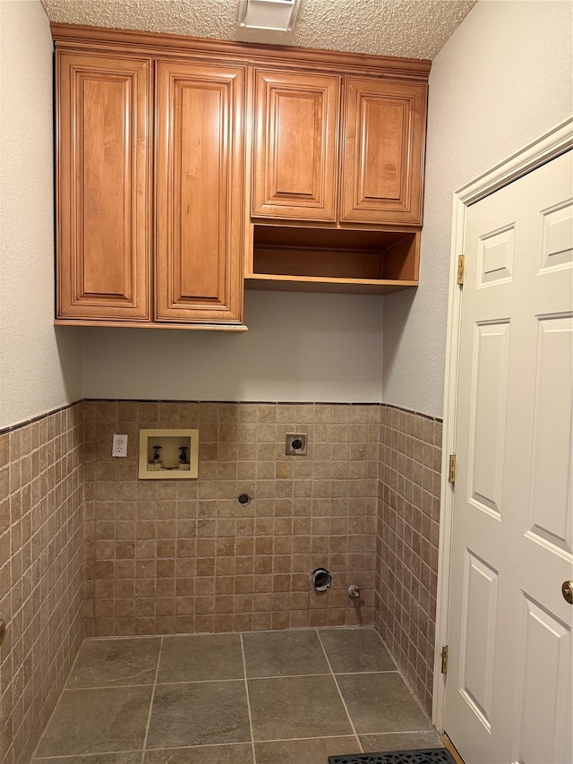 laundry area featuring hookup for a washing machine, hookup for an electric dryer, a textured ceiling, tile walls, and cabinets