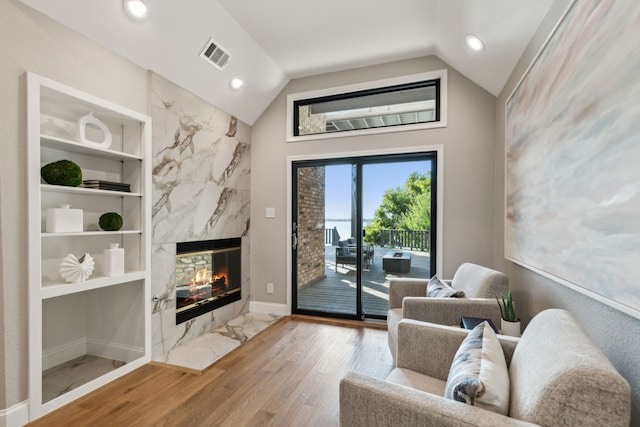 living room with lofted ceiling, wood-type flooring, and a high end fireplace