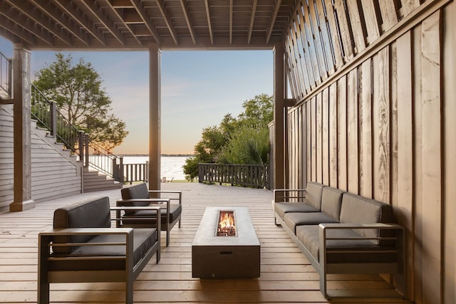 deck at dusk featuring a water view and an outdoor living space with a fire pit