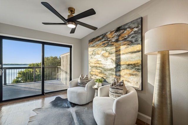 sitting room featuring a water view, hardwood / wood-style floors, and ceiling fan