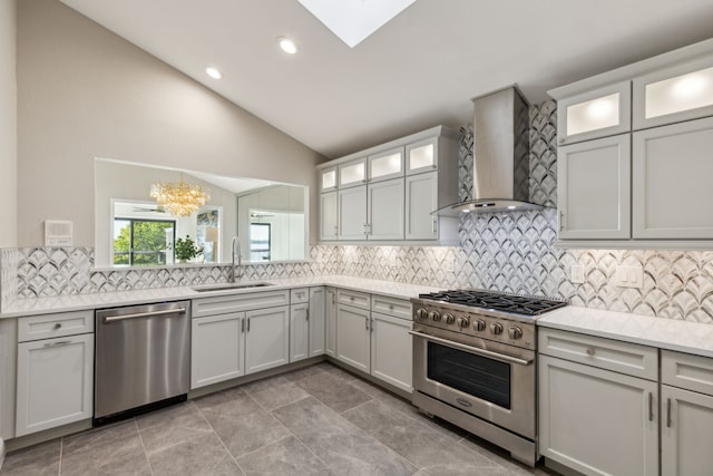 kitchen with sink, wall chimney exhaust hood, stainless steel appliances, lofted ceiling with skylight, and an inviting chandelier