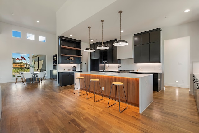 kitchen featuring hanging light fixtures, sink, a center island with sink, a kitchen breakfast bar, and light hardwood / wood-style floors