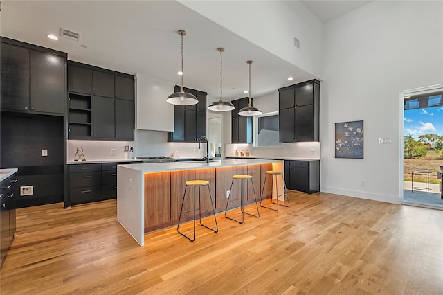 kitchen with light hardwood / wood-style floors, a kitchen bar, decorative light fixtures, a center island with sink, and sink