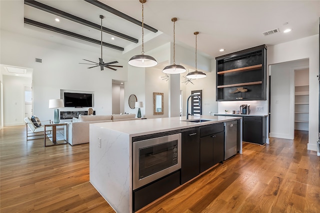 kitchen with an island with sink, sink, stainless steel appliances, a fireplace, and hardwood / wood-style floors