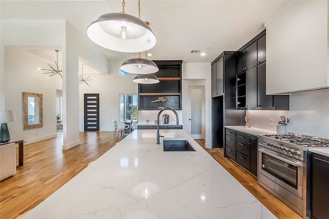 kitchen with light wood-type flooring, light stone counters, sink, hanging light fixtures, and high end stainless steel range