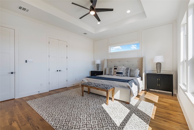 bedroom with ceiling fan, a raised ceiling, and wood-type flooring