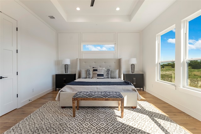 bedroom featuring ceiling fan, light hardwood / wood-style flooring, and a tray ceiling