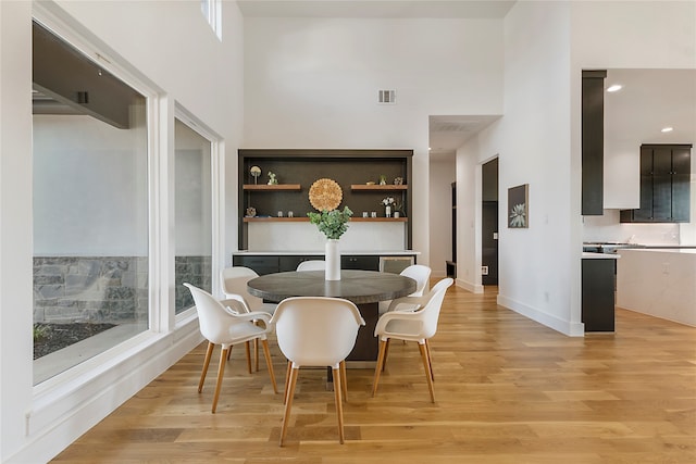 dining space with light wood-type flooring, a high ceiling, and a healthy amount of sunlight