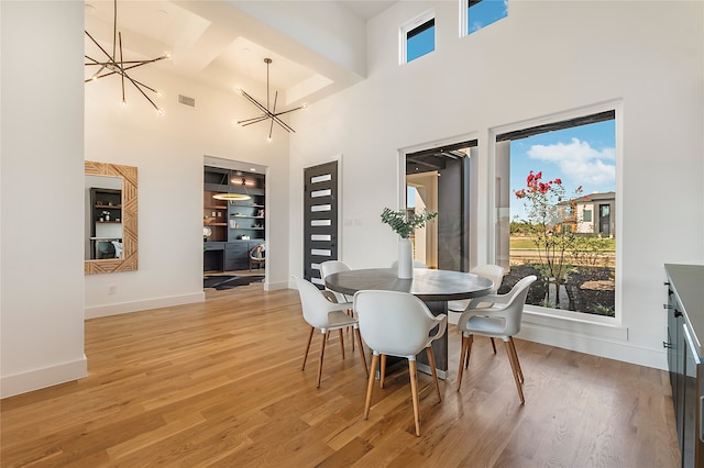 dining area with a notable chandelier, a high ceiling, wood-type flooring, and a healthy amount of sunlight