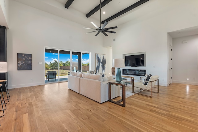 living room with light hardwood / wood-style flooring, a high ceiling, ceiling fan, and beamed ceiling