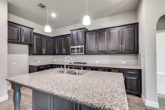 kitchen featuring a center island with sink, sink, pendant lighting, and light stone countertops