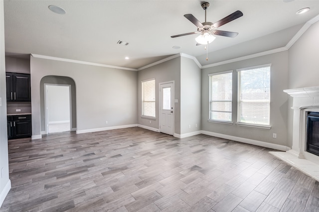 unfurnished living room with light hardwood / wood-style floors, ornamental molding, ceiling fan, and a high end fireplace