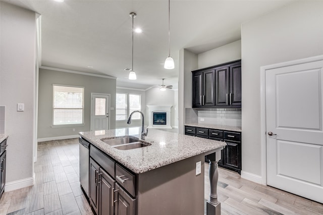 kitchen with ceiling fan, light stone counters, an island with sink, sink, and stainless steel dishwasher