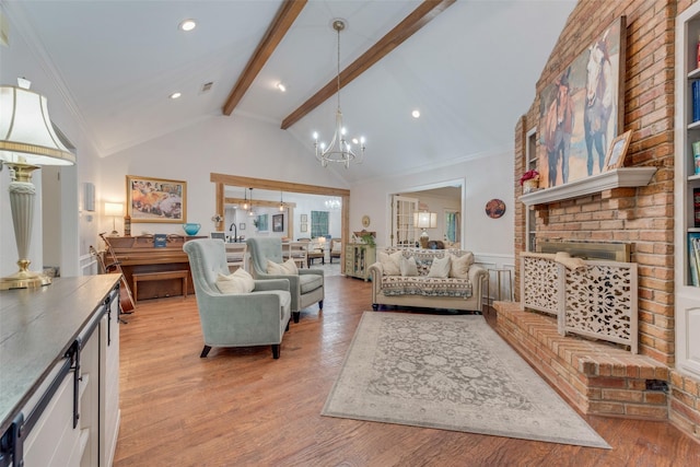 living room featuring vaulted ceiling with beams, an inviting chandelier, a brick fireplace, and light hardwood / wood-style floors