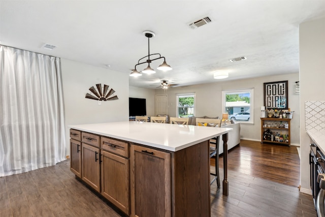 kitchen featuring pendant lighting, a breakfast bar area, dark wood-type flooring, ceiling fan, and a center island