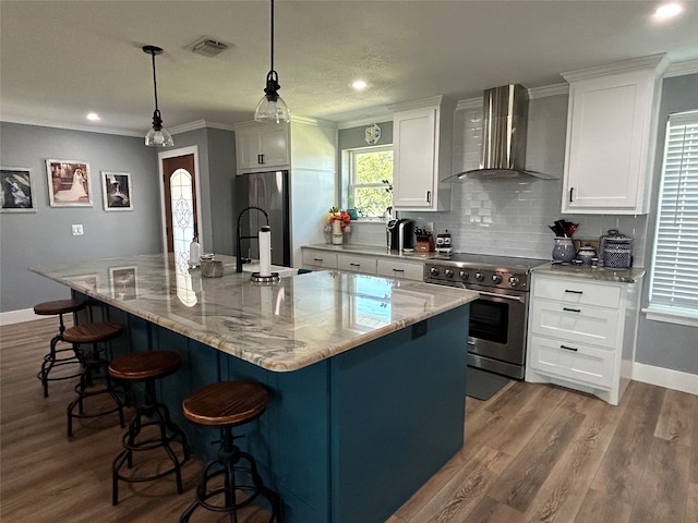 kitchen featuring decorative light fixtures, appliances with stainless steel finishes, wall chimney exhaust hood, and a large island