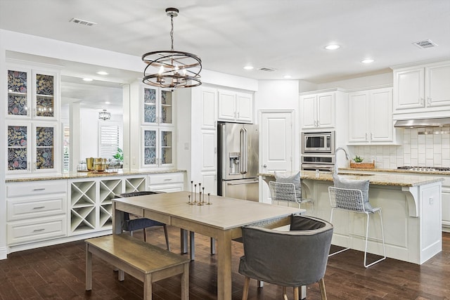 kitchen with light stone countertops, decorative backsplash, stainless steel appliances, decorative light fixtures, and white cabinetry