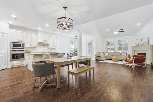 dining space with dark hardwood / wood-style floors, ceiling fan with notable chandelier, and vaulted ceiling