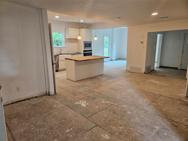 kitchen featuring white cabinets, a kitchen island, appliances with stainless steel finishes, decorative light fixtures, and wooden counters