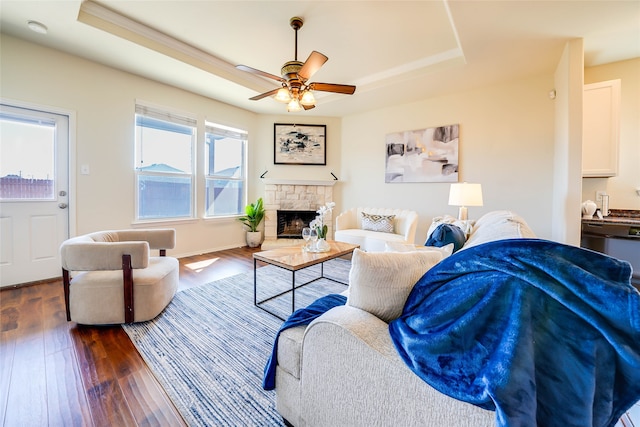 living room featuring ceiling fan, a fireplace, a raised ceiling, and dark wood-type flooring