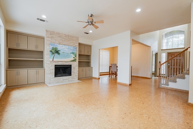 unfurnished living room featuring built in features, ceiling fan, and a stone fireplace