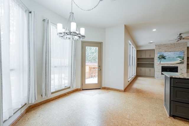 unfurnished dining area featuring ceiling fan with notable chandelier and a fireplace