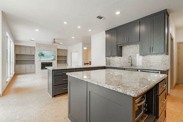 kitchen with light stone counters, kitchen peninsula, a kitchen island, a large fireplace, and ceiling fan