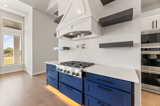 kitchen featuring appliances with stainless steel finishes, blue cabinets, light hardwood / wood-style floors, and white cabinets