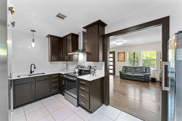 kitchen with pendant lighting, dark brown cabinetry, wall chimney exhaust hood, stainless steel appliances, and sink