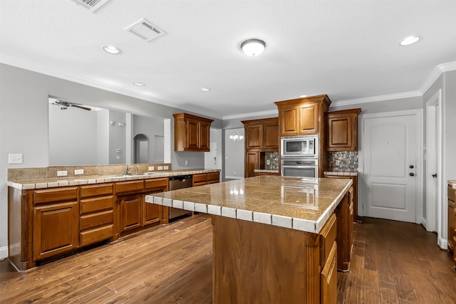 kitchen featuring a kitchen island, a kitchen breakfast bar, appliances with stainless steel finishes, hardwood / wood-style floors, and crown molding