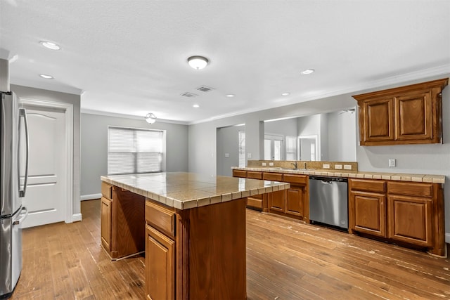 kitchen with ornamental molding, a kitchen island, appliances with stainless steel finishes, tile countertops, and hardwood / wood-style floors