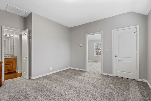 unfurnished bedroom with vaulted ceiling, ensuite bath, and light carpet