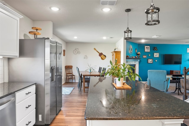 kitchen with appliances with stainless steel finishes, light wood-type flooring, a fireplace, pendant lighting, and white cabinets