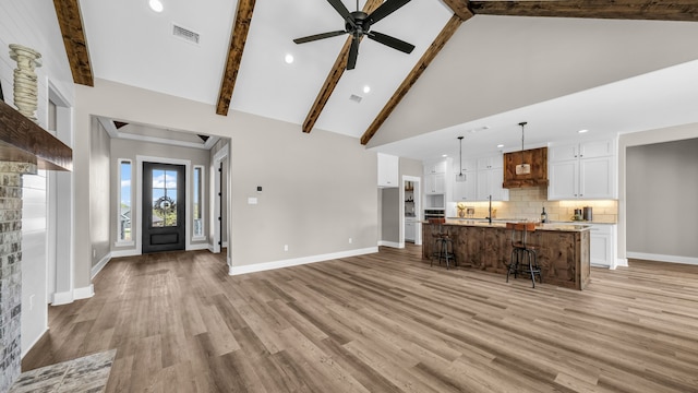 unfurnished living room with light hardwood / wood-style flooring, beam ceiling, ceiling fan, and high vaulted ceiling