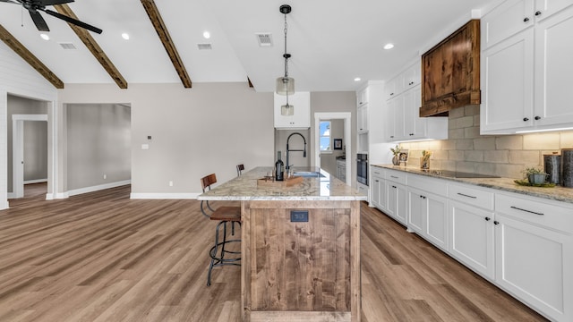 kitchen with hanging light fixtures, lofted ceiling with beams, an island with sink, and white cabinetry