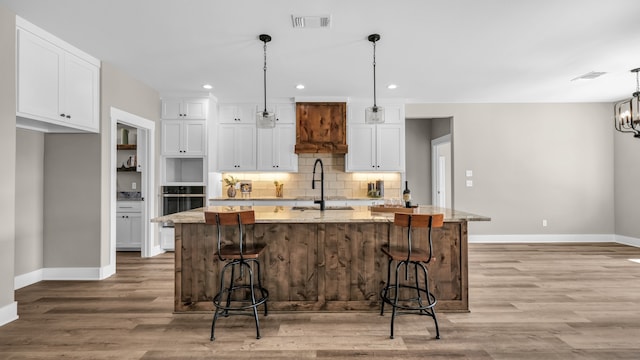 kitchen with pendant lighting, white cabinets, a kitchen island with sink, a breakfast bar, and light stone countertops